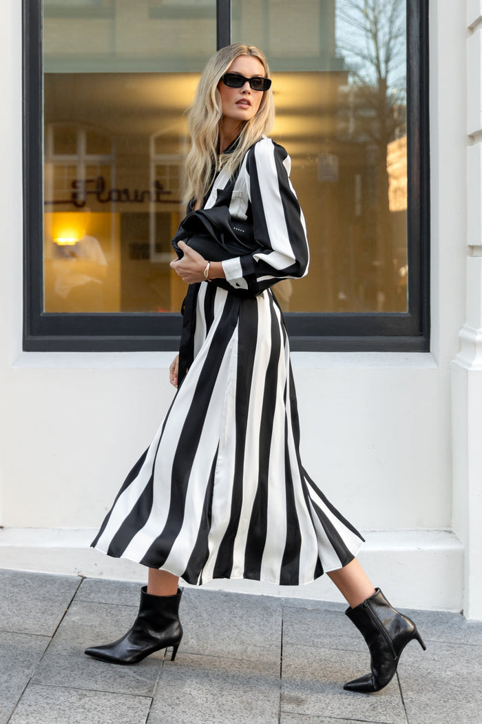 Woman wearing a black and white striped dress standing in front of a building with large windows.