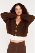 Woman wearing a brown cropped sweater with gold buttons on a white background
