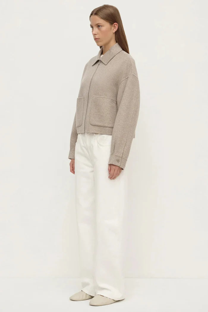 Woman wearing a beige jacket and white pants on a light gray background