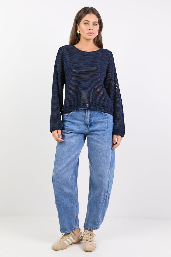 Woman wearing a navy sweater and light blue jeans on a white background