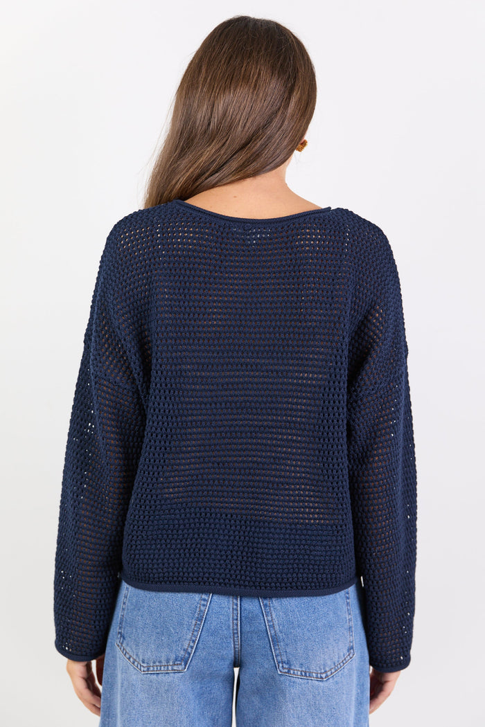 Person wearing a navy blue knitted sweater and light blue jeans on a white background