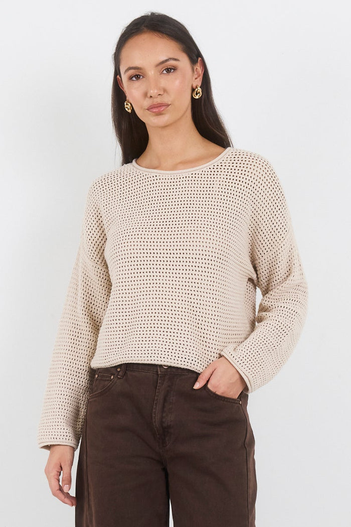 Woman wearing a beige sweater and brown pants on a white background