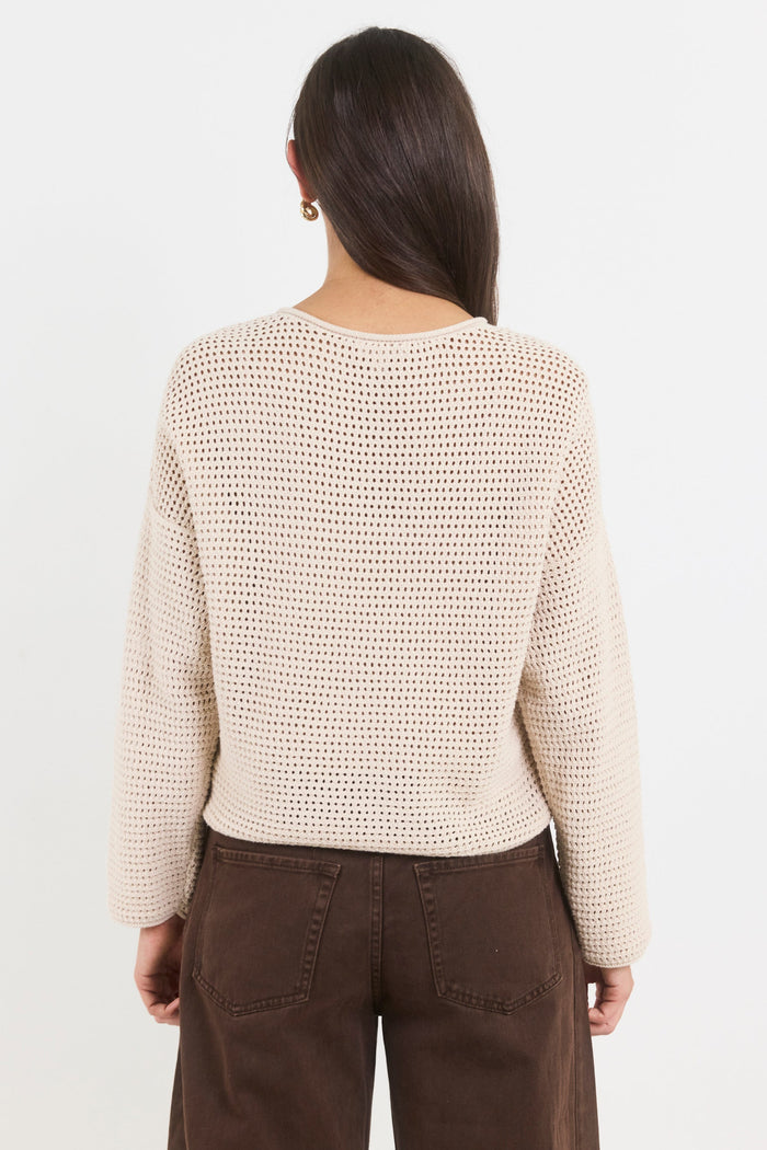 Person wearing a beige knitted sweater and brown pants on a white background