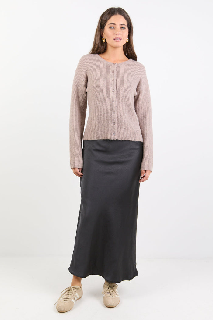 Woman wearing a beige cardigan and black skirt on a white background