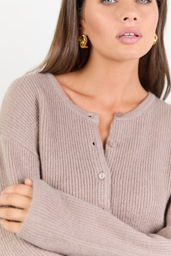 Woman wearing a beige ribbed sweater with a plain background