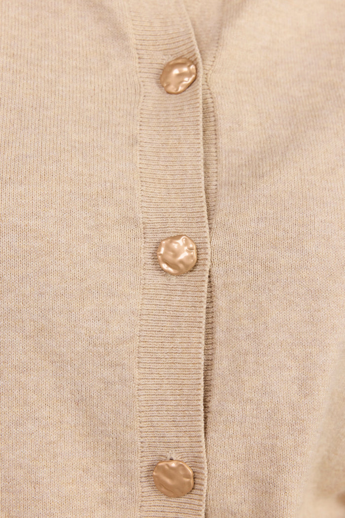 Close-up of a light beige knit cardigan with a vertical ribbed placket and four metallic gold buttons.