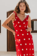 Woman wearing a red dress with white polka dots in an outdoor setting.