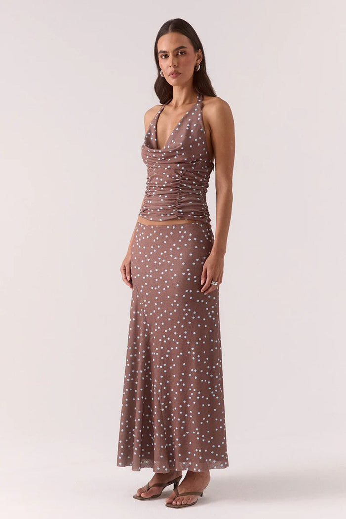 Woman wearing a ruched halter neck top in brown and blue polka dots with the matching skirt