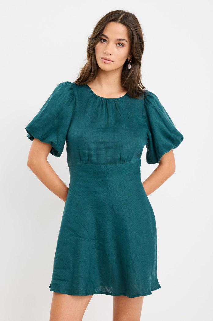 Woman wearing a forest green mini dress with puff sleeves, bias-cut shape, and fitted waist, styled simply for an elegant look.
