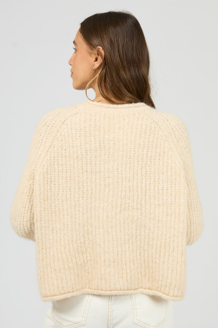 Woman wearing a beige knitted cardigan on a plain background
