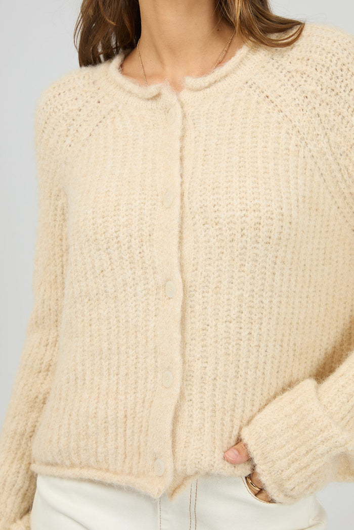 Beige knitted cardigan worn by a person on a light gray background