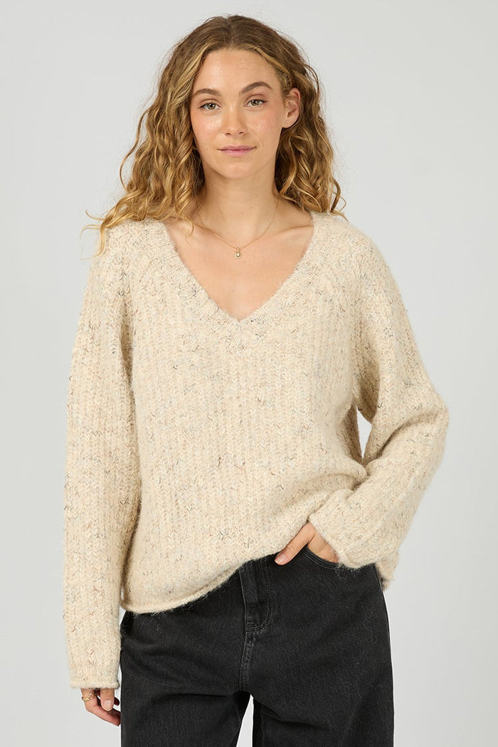 Woman wearing a beige sweater and black pants on a white background
