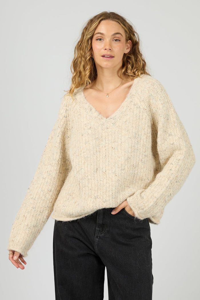 Woman wearing a cream sweater and black pants against a plain background