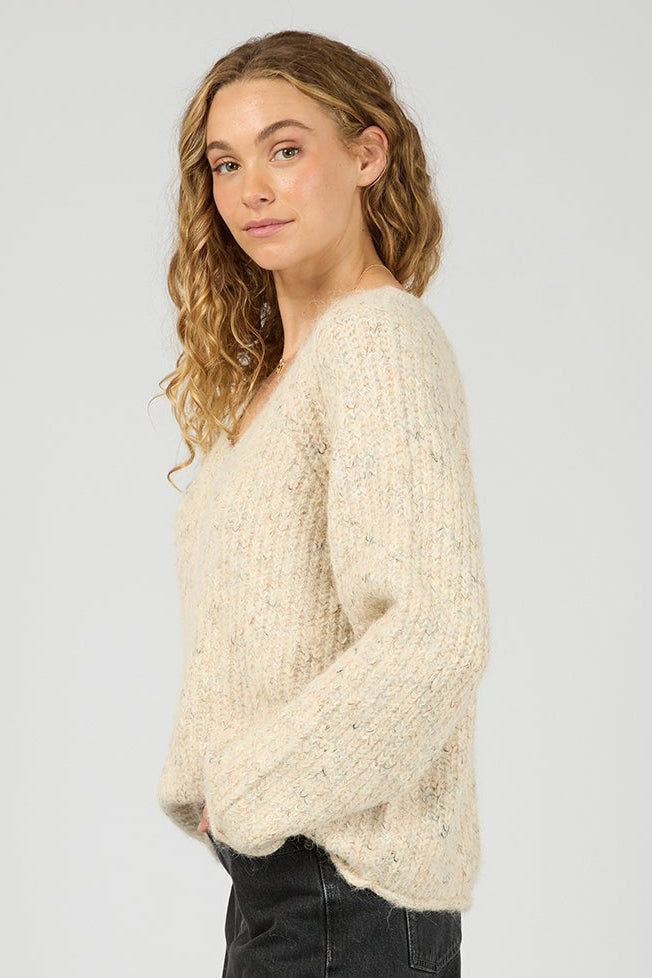 Woman wearing a cream sweater and black pants on a white background