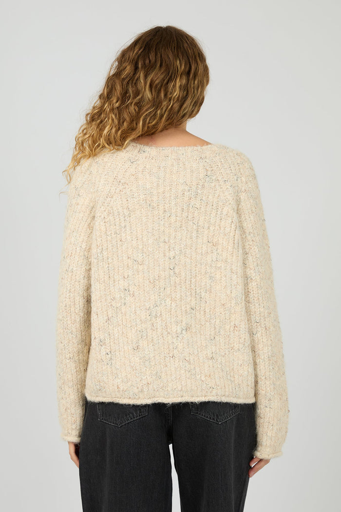 Woman wearing a cream sweater with a plain background