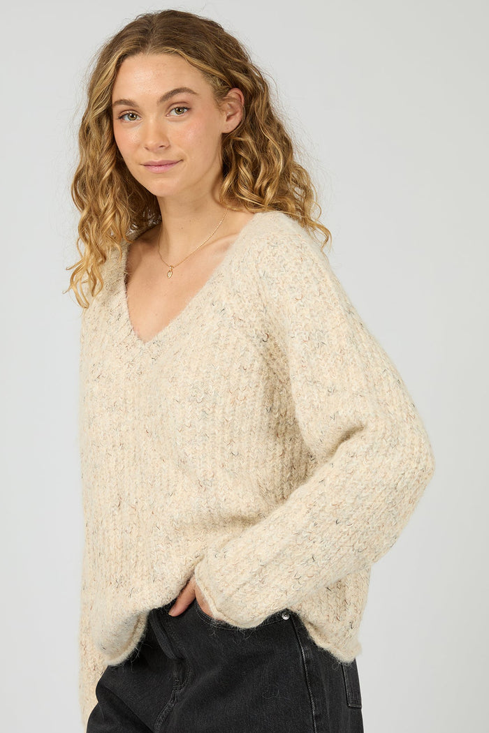 Woman wearing a cream knitted sweater and dark jeans on a light gray background