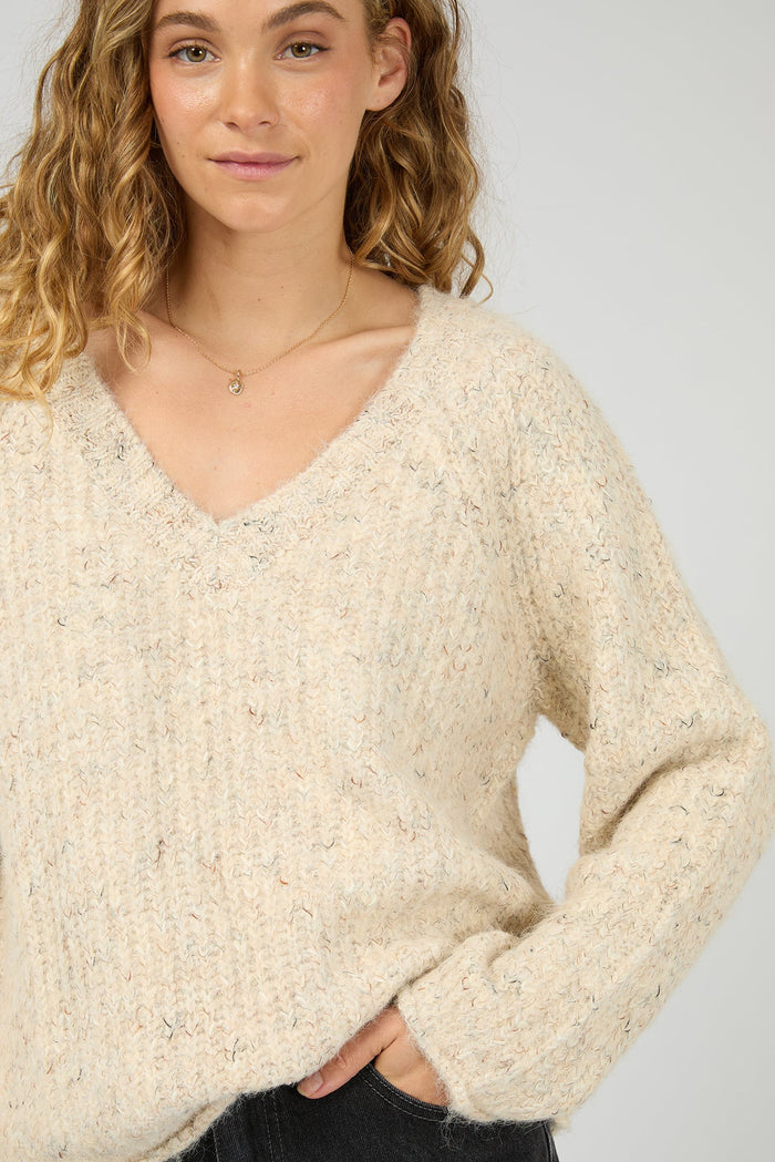 Woman wearing a beige sweater against a plain background