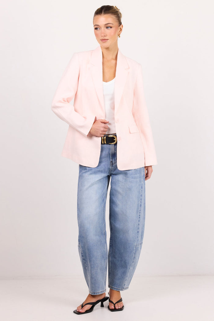 A woman modeling a light pink blazer, light-wash wide-leg blue jeans, a white top, and black sandals against a plain white studio background.