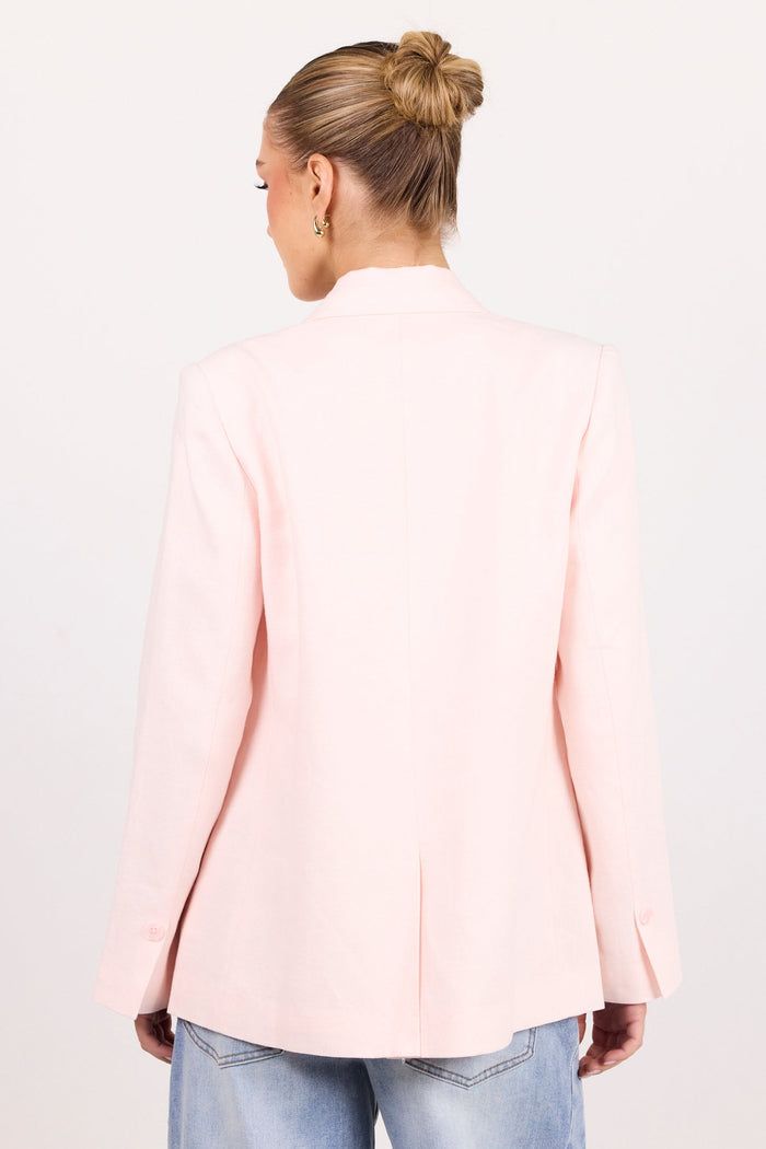 A woman viewed from behind wearing a light pink blazer and blue jeans against a plain white studio background.
col_pattern