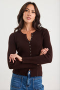 Woman wearing a brown ribbed sweater with buttons and blue jeans on a white background