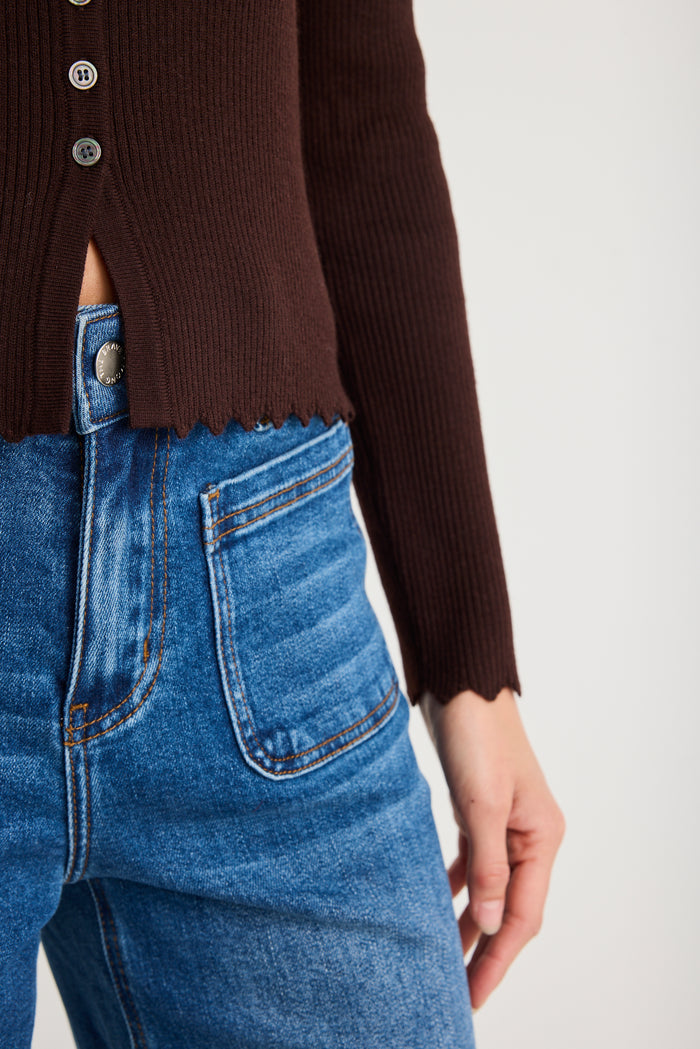 Person wearing a brown cardigan and blue jeans on a light gray background