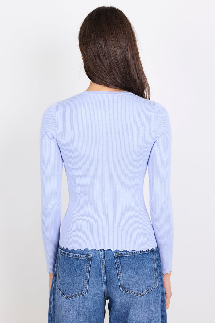Person wearing a light blue long-sleeve top and blue jeans on a white background