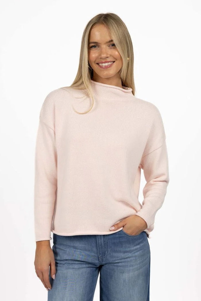 Woman wearing a light pink sweater and blue jeans on a white background