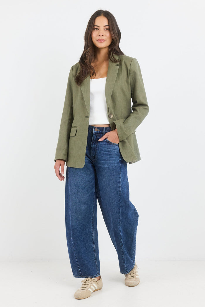 Woman wearing a green blazer, white top, and blue jeans on a white background