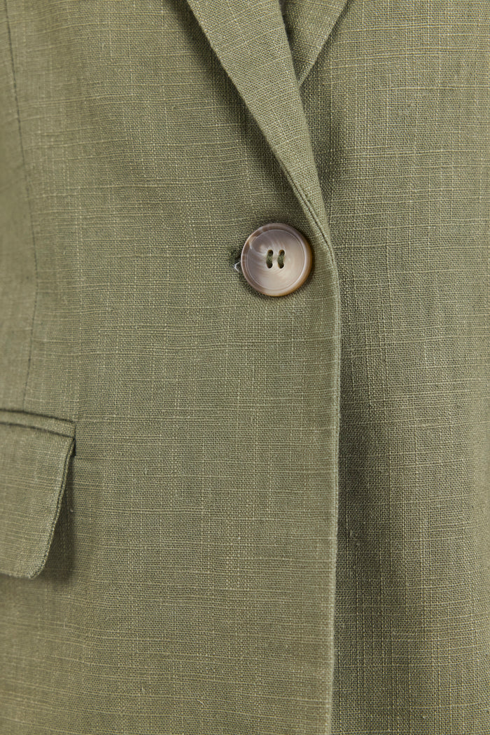 Close-up of a green blazer with a button on a matching fabric background