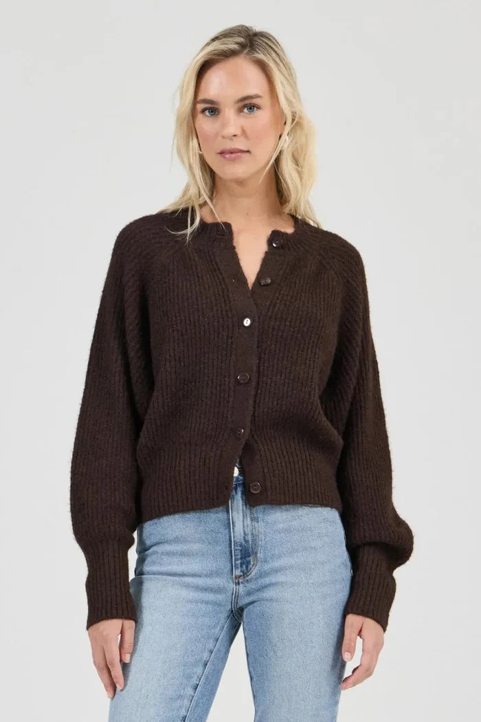 Woman wearing a brown cardigan and light blue jeans on a white background