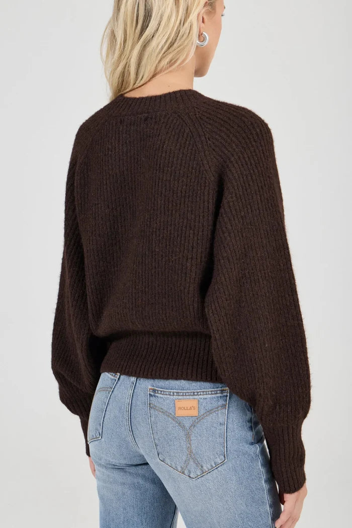 Person wearing a brown sweater and light blue jeans on a plain background