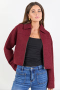 Woman wearing a maroon jacket, black top, and blue jeans on a white background