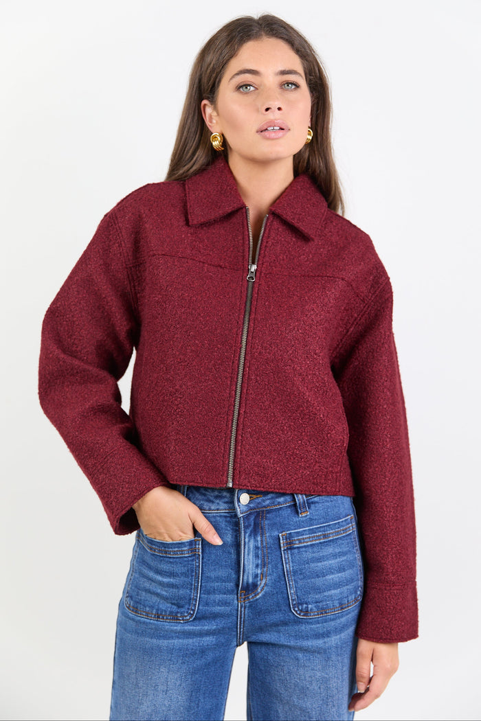 Woman wearing a burgundy jacket and blue jeans on a white background