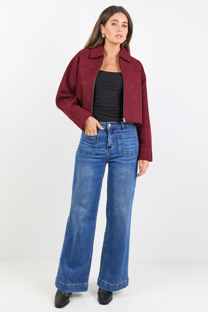 Woman wearing a burgundy jacket, black top, and blue jeans on a white background