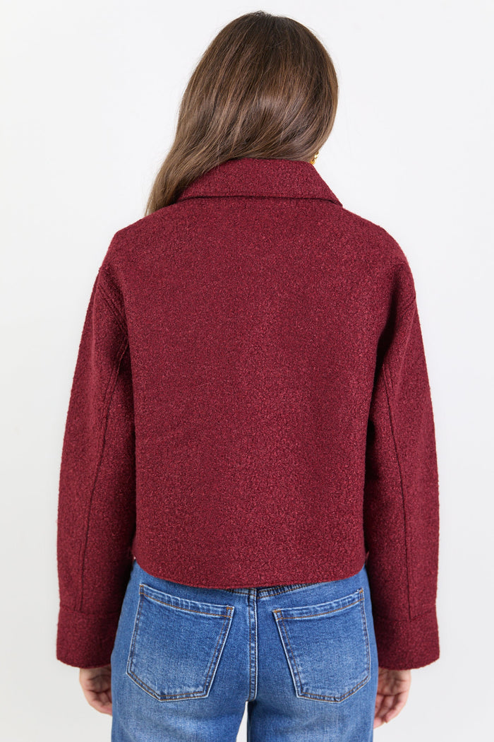 Person wearing a burgundy jacket and blue jeans on a white background