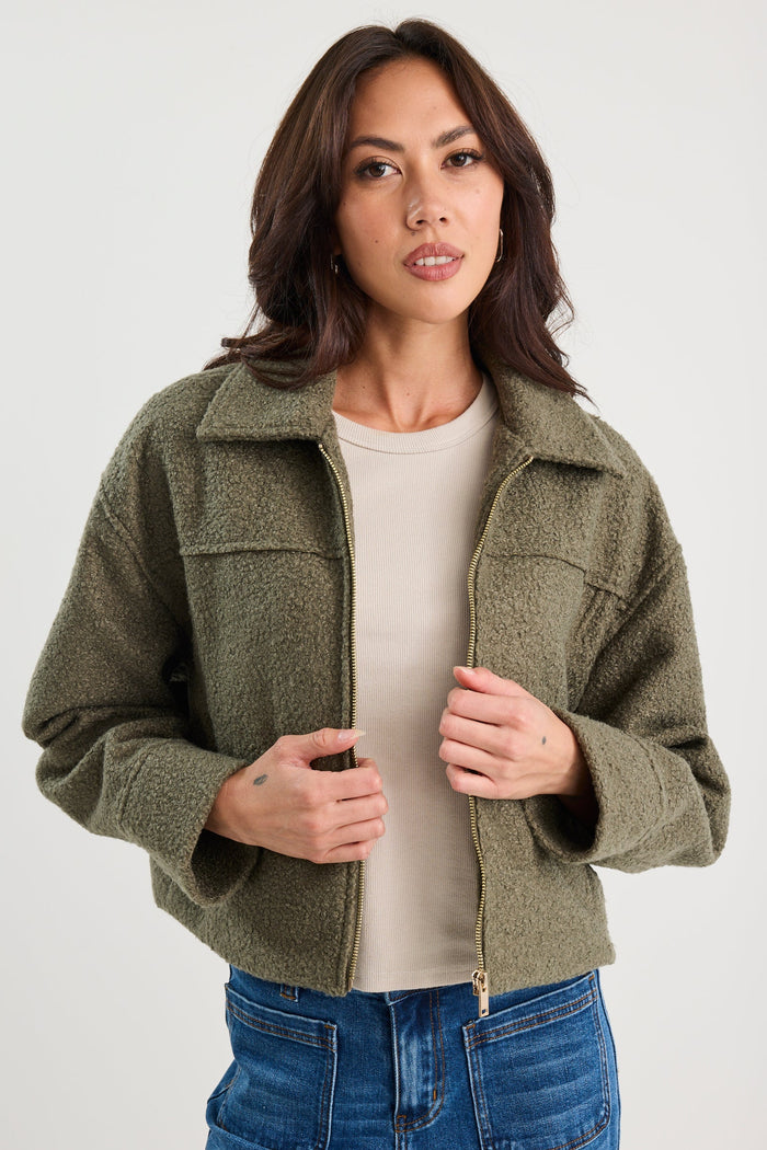 Woman wearing a green jacket over a white shirt and blue jeans on a white background