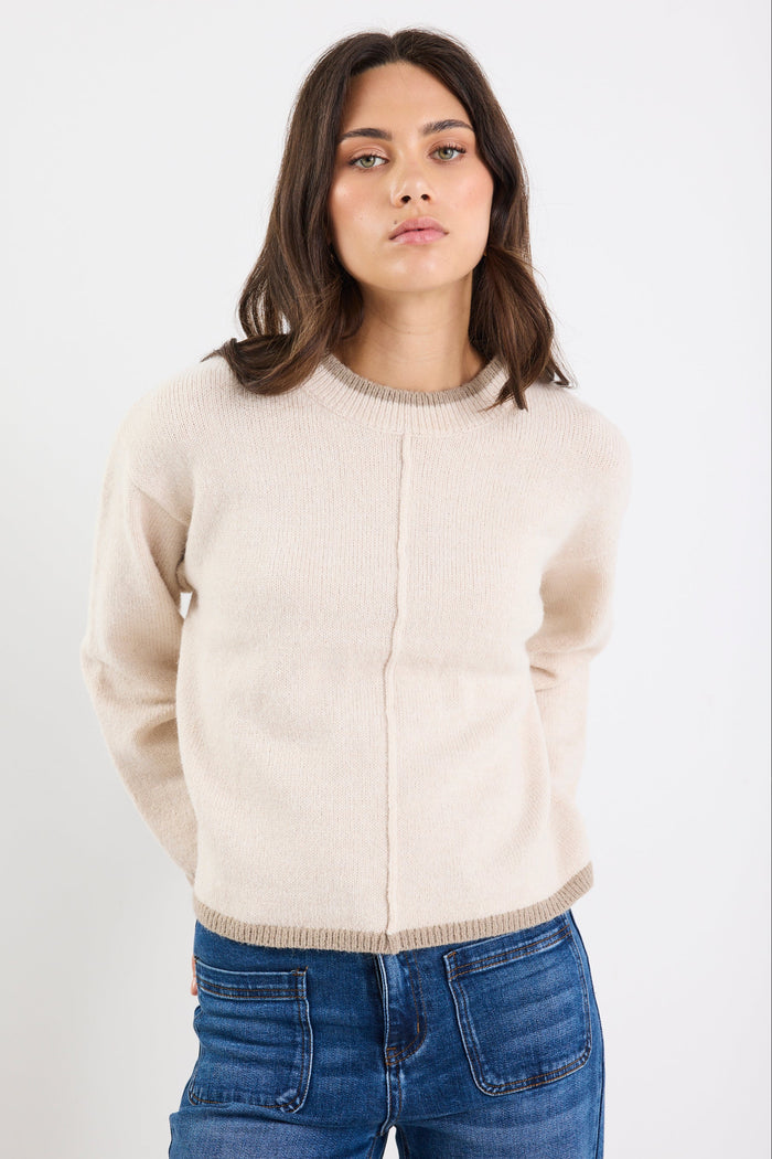 Woman wearing a beige sweater and blue jeans on a white background