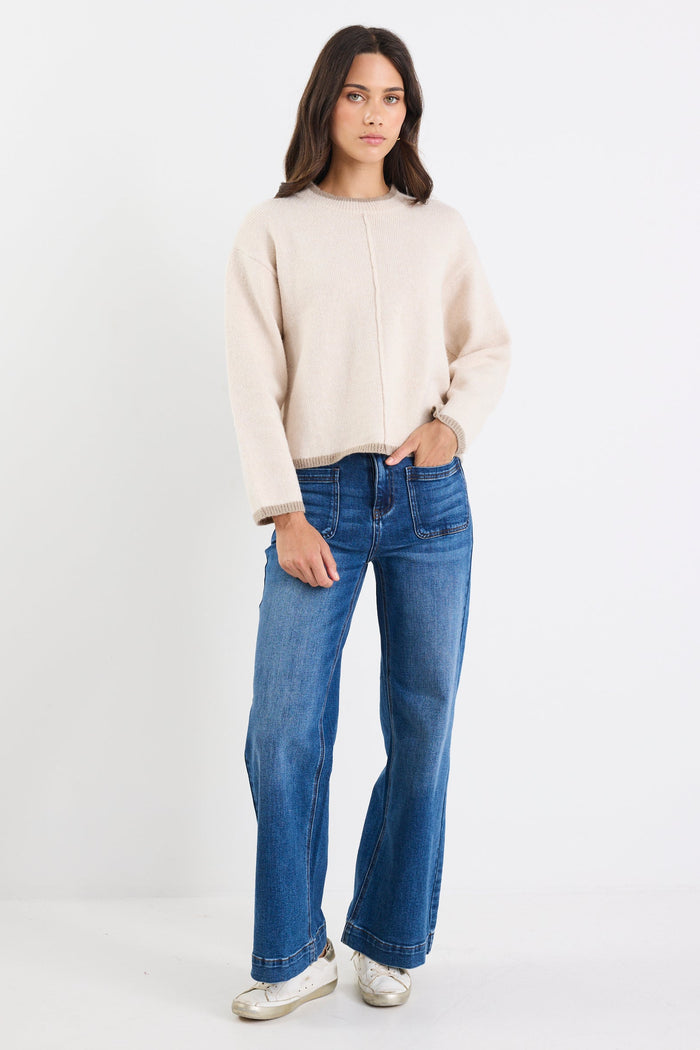 Woman wearing a beige sweater and blue jeans on a white background