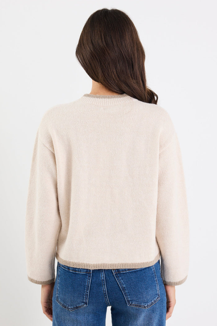 Person wearing a cream sweater and blue jeans on a white background