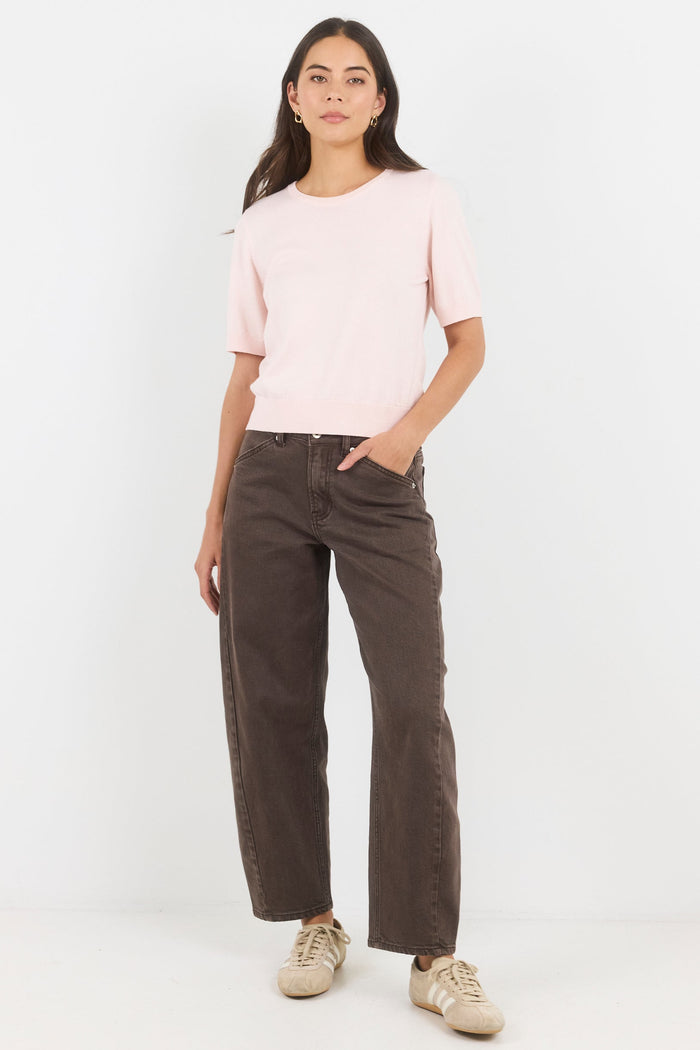 Woman wearing a light pink top and dark brown pants on a white background
