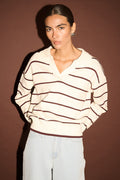 Woman wearing a striped sweater and light jeans against a brown background