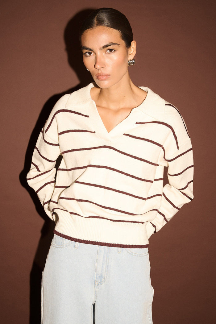 Woman wearing a striped sweater and light jeans against a brown background
