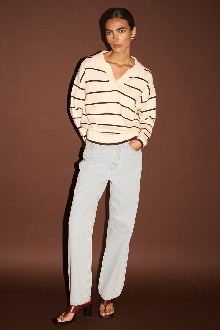 Woman wearing a striped sweater and white pants against a brown background