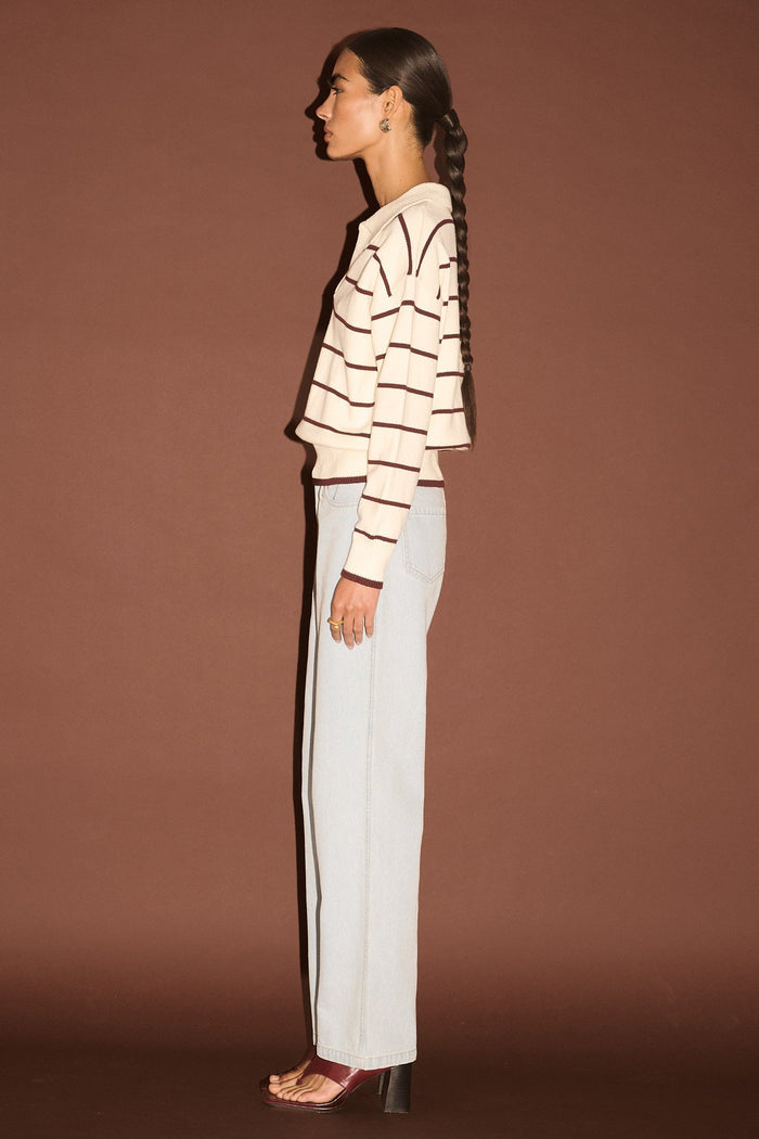 Woman wearing a striped sweater and white pants against a brown background
