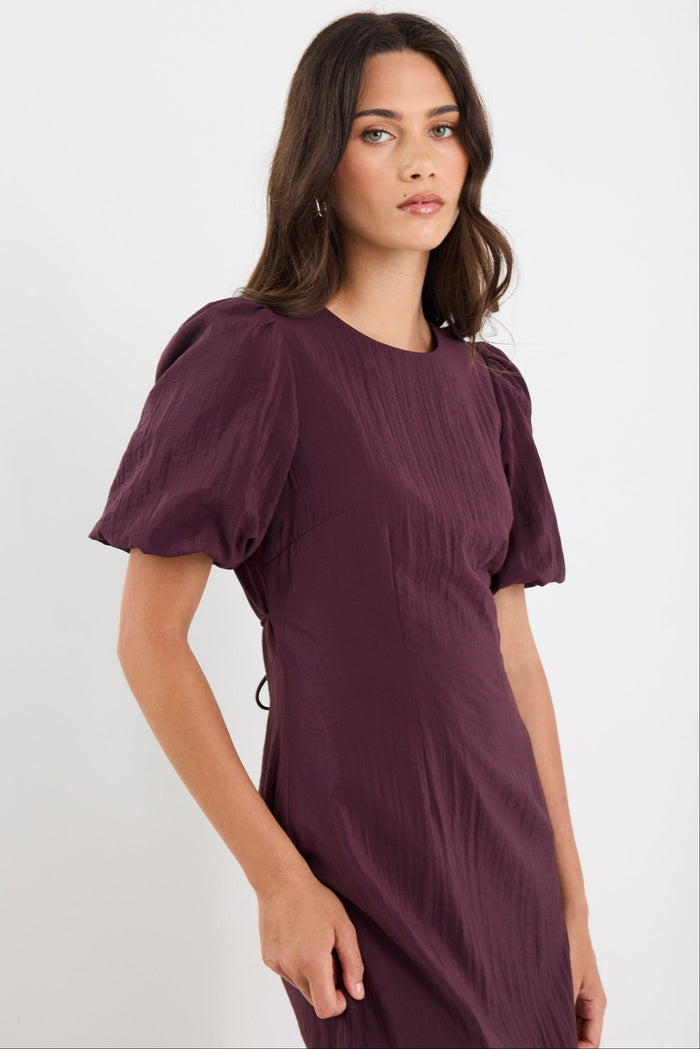 Woman wearing a purple dress with puffed sleeves against a white background
