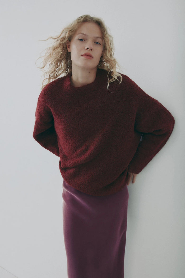 Woman wearing a burgundy sweater and skirt against a white background