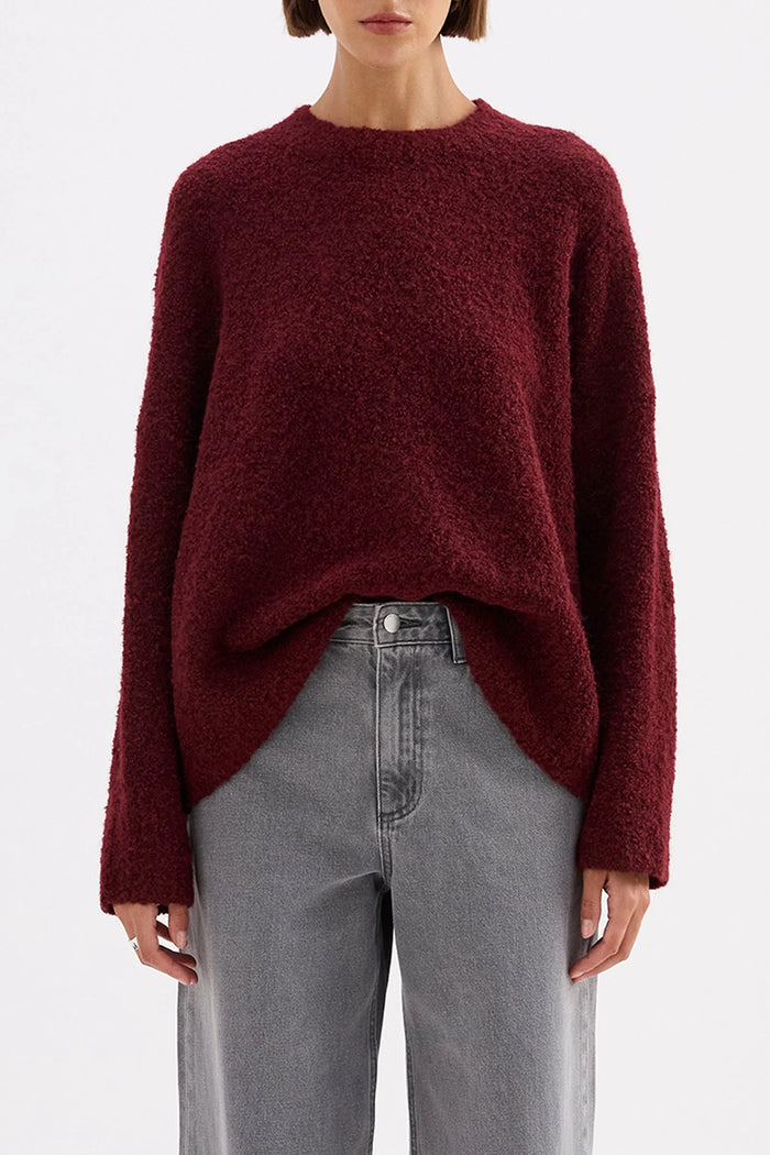 Person wearing a burgundy sweater and gray pants on a white background