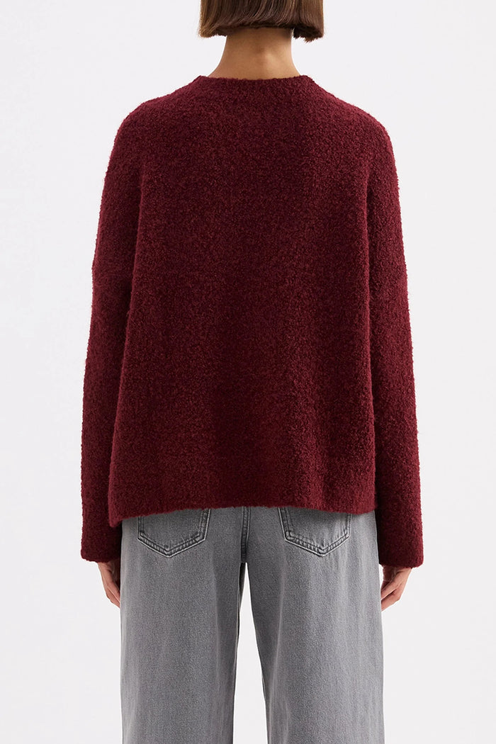 Person wearing a burgundy sweater and gray pants on a white background
