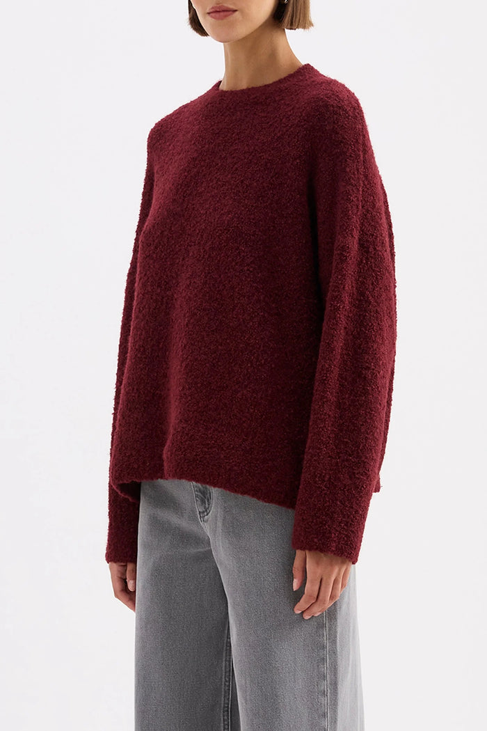 Person wearing a burgundy sweater and gray pants on a white background