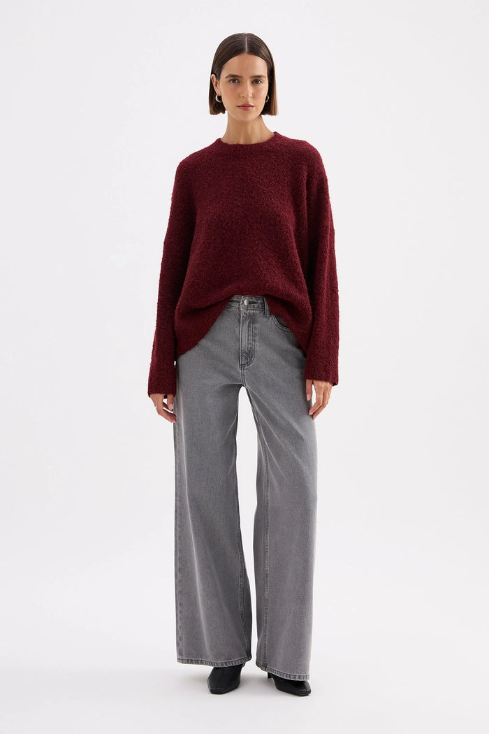 Person wearing a burgundy sweater and gray pants on a white background